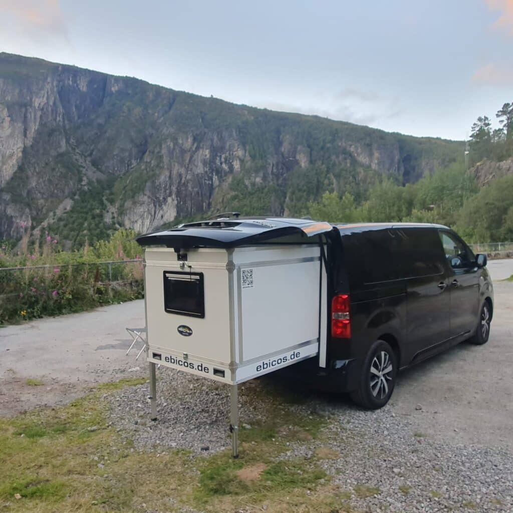 Toyota Proace Verso mit Ausziehmodul von ebicos.de auf einem Bergparkplatz mit beeindruckender Felskulisse – kompaktes Schlafsystem für Reisen in der Natur.
